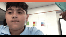 a boy in a blue shirt looks at the camera in front of a wall with posters on it including one that says " structure "