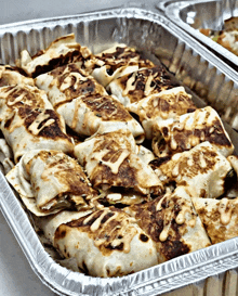 aluminum foil tray filled with burritos with sauce on top