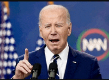 a man in a suit and tie is giving a speech in front of microphones .