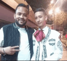 a man in a mariachi outfit is posing for a picture with another man in a black vest .