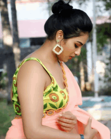 a woman wearing a pink saree and a green blouse with square earrings