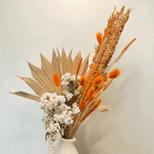 a vase filled with dried flowers and leaves against a white wall