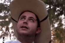 a man wearing a cowboy hat and a white shirt is looking up at the sky .