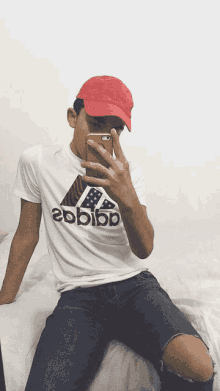 a young man is taking a selfie with his phone while wearing a red hat and an adidas shirt