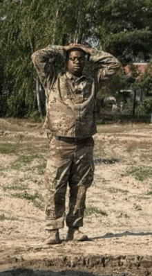 a man in a military uniform stands in the dirt with his hands on his head