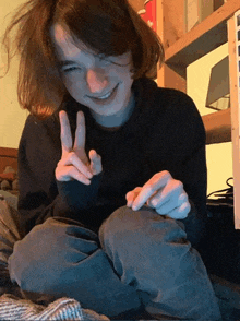 a young man is giving a peace sign while sitting on a bed