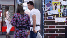 a man and a woman are walking in front of a brick wall with posters on it including one that says ray ganador