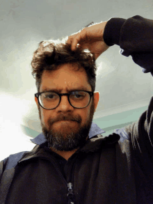 a man with glasses and a beard is scratching his hair