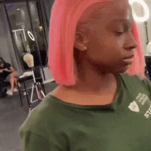 a woman with pink hair and a green shirt is standing in a salon .