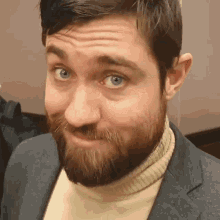 a man with a beard wearing a turtleneck and a suit makes a funny face