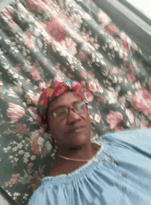 a woman wearing glasses and a head scarf is laying on a floral curtain