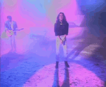 a man is playing a guitar and a woman is standing in front of a car in a purple light .