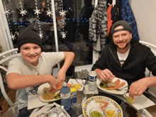 a man and a boy are sitting at a table with plates of food and a can of budweiser