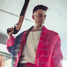 a man in a pink and blue jacket holds a shotgun