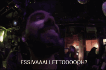 a man with a beard is smiling in a dark room with the words " essivaaaellettooooh " written above him