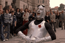 a man in a silver costume with a red rose on his chest is standing in front of a crowd of people