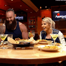 a man and a woman are sitting at a table with plates of food in front of an applebee 's sign