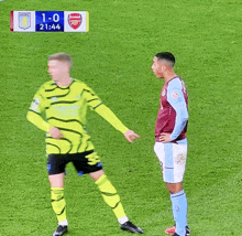 two soccer players are standing on a field with the score 1-0