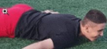 a man in a black shirt and red shorts is laying on his back on a soccer field .