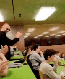 a group of people are sitting at green tables in a classroom and applauding .