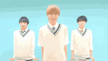 three boys in school uniforms are standing in front of a blue background