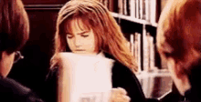 a woman is holding a piece of paper in front of her face while sitting in front of a bookshelf .