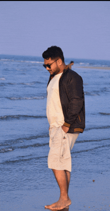 a man standing on a beach wearing sunglasses and a black jacket