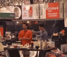 a man in a red shirt is standing in front of a table with a sign that says licious fresh meats and seafood .