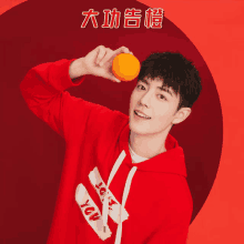 a man in a red hoodie is holding an orange in his hand