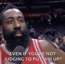 a basketball player with a beard is talking into a microphone while sitting in the stands during a game .