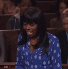 a woman in a blue and white polka dot shirt smiles in a courtroom