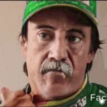 a man with a mustache wearing a green hat and a green shirt is making a funny face .