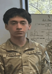 a young man in a us army uniform is standing in front of a whiteboard