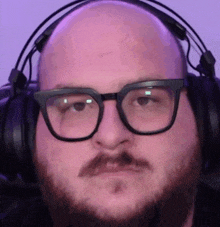 a bald man wearing glasses and headphones looks at the camera