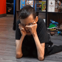 a man wearing glasses is sitting on the floor in front of a shelf with holcomb in the middle books