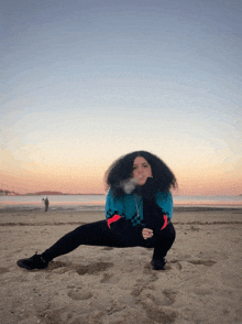 a woman with curly hair is squatting on a beach smoking a cigarette