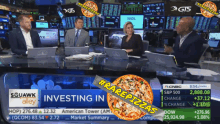 a group of people are sitting at a table with a pizza in front of them and a sign that says investing in