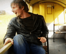 a man in a black jacket is laughing while sitting on a railing