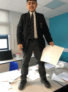 a boy in a school uniform holds a piece of paper in front of a blue wall