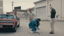 a man kneeling down with a gun in front of a red car with a license plate that says ' nv '