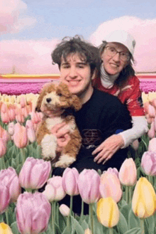 a man and woman holding a puppy in front of a field of flowers