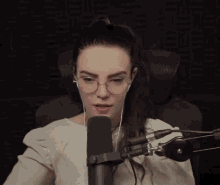 a woman wearing glasses is sitting in front of a microphone and talking into it .