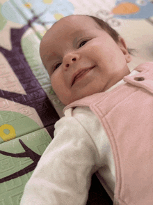 a baby in a pink vest is laying on a mat with a penguin on it