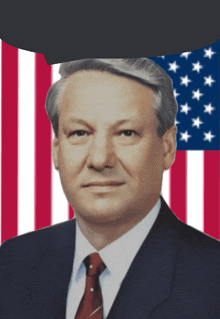 a man in a suit and tie stands in front of a flag