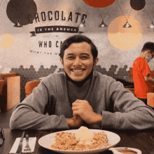 a man sitting at a table with a plate of food and a sign that says chocolate is the answer