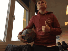 a young man wearing a maroon sweatshirt that says ' norwegian football club ' on the back gives a thumbs up