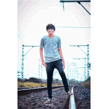 a young man standing on train tracks wearing a grey shirt