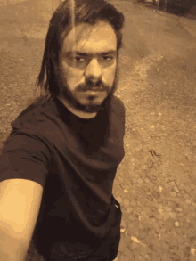 a man with long hair and a beard is taking a selfie on a cobblestone street