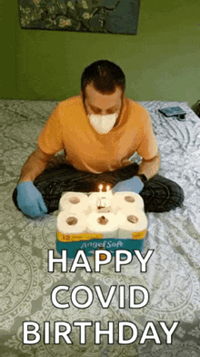 a man wearing a mask and gloves is sitting on a bed with a birthday cake made out of toilet paper .