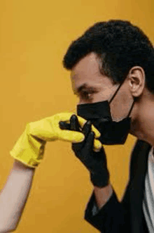 a man wearing a mask is kissing a woman 's hand while wearing yellow gloves .